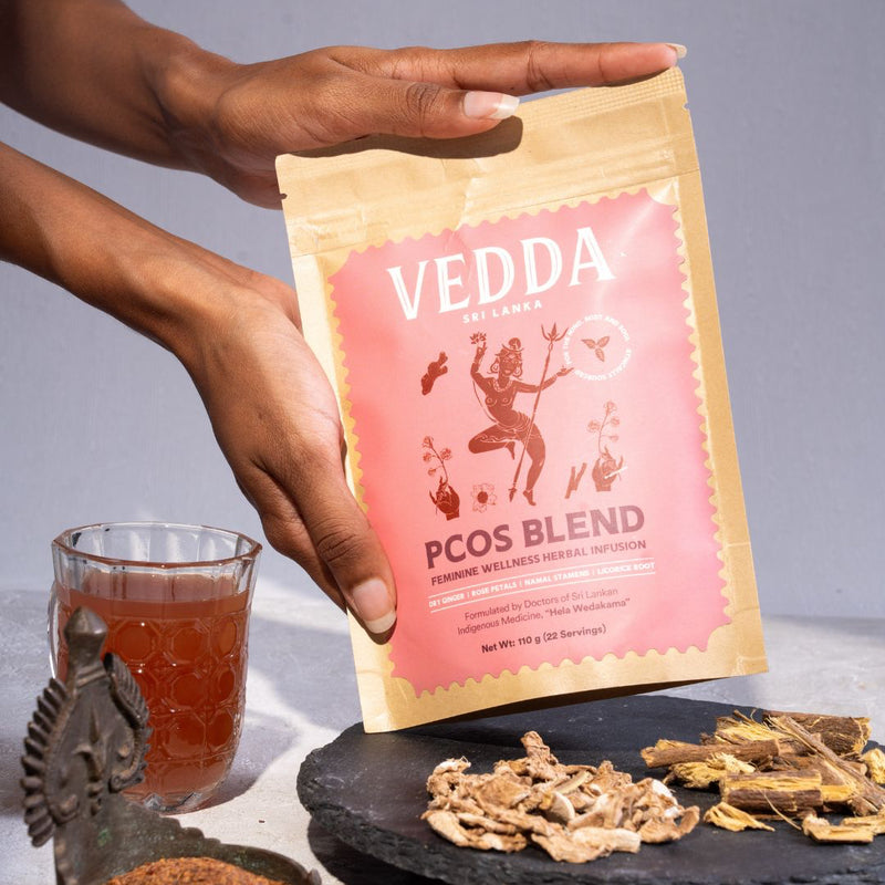 A person holds a stand-up pouch of VEDDA PCOS Blend herbal tea. The pouch is pink and beige with a central illustration of a dancing figure.