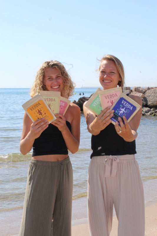 two women standing on the beach, holding pouches 'Vedda' tea