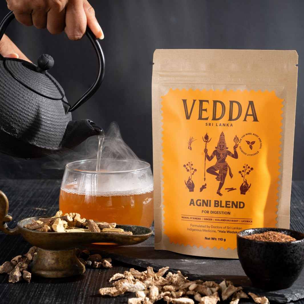 Tea being poured into a glass with a Vedda Agni Blend tea package in the background.