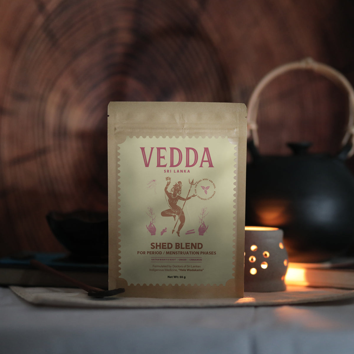 A stand-up pouch of VEDDA by SINGAPORE Shed Blend herbal tea, set against a warm, rustic background with a teapot and candlelight.